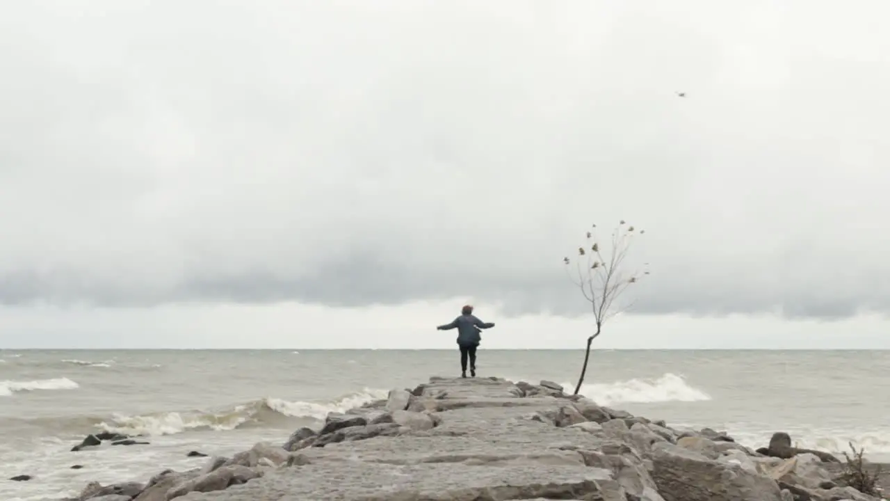 Lonely woman standing pensively at the end of a stone breakwater on a stormy day