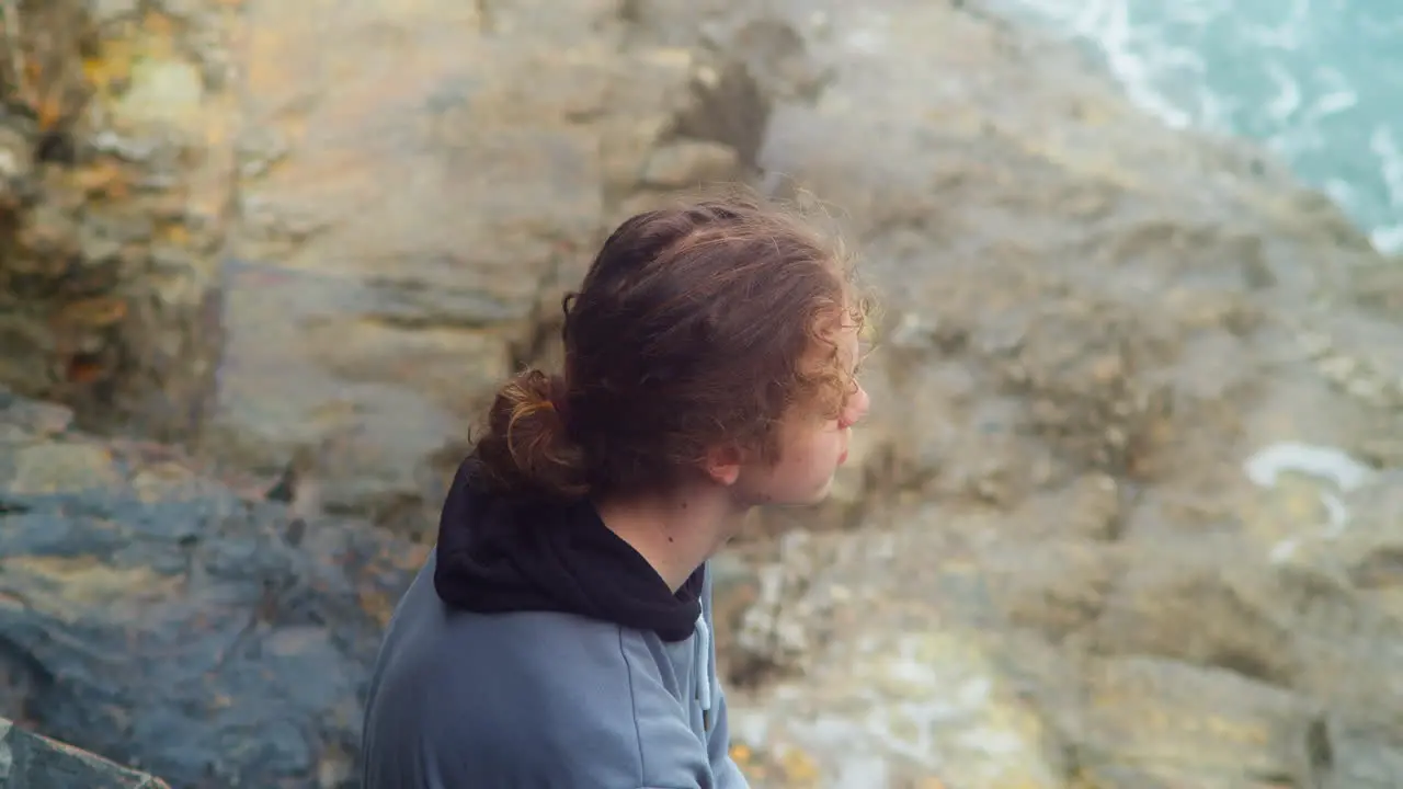 Thoughtful Young Teenager Lad Sitting on a Rock Watching Ocean Breaking Waves