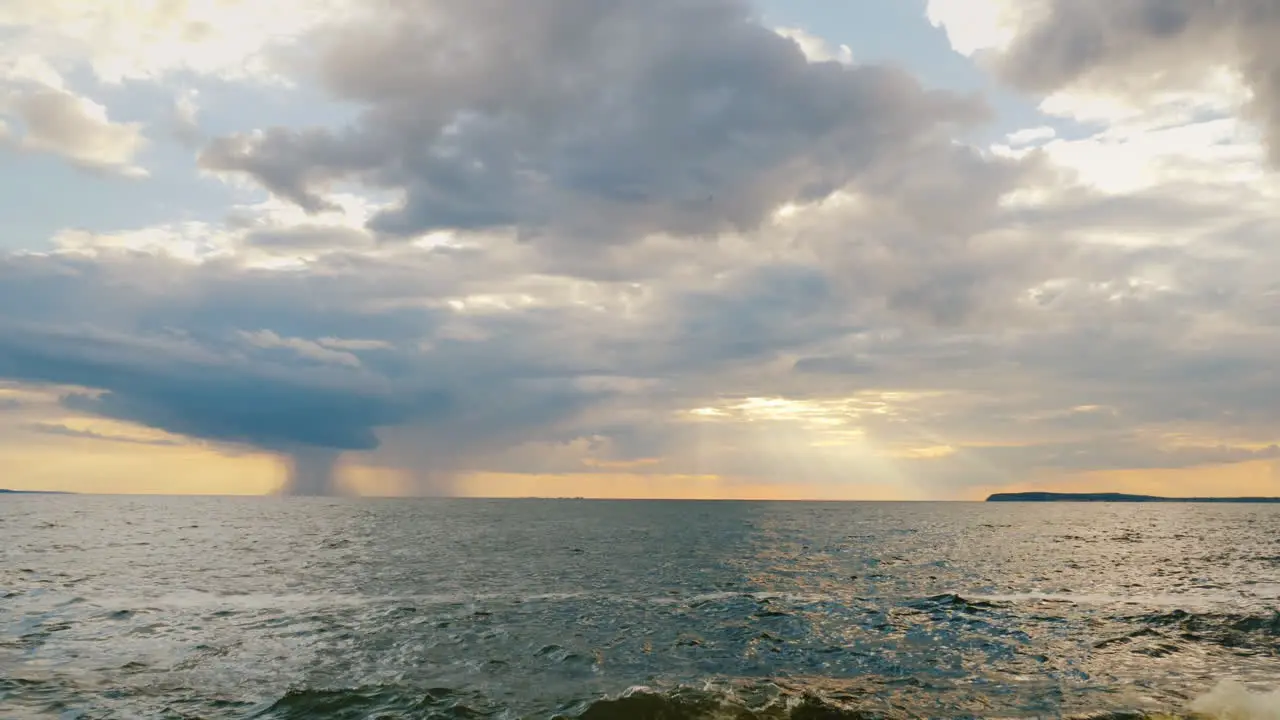 A Rain Cloud With Rain Over The Sea And A Setting Sun With Beautiful Rays