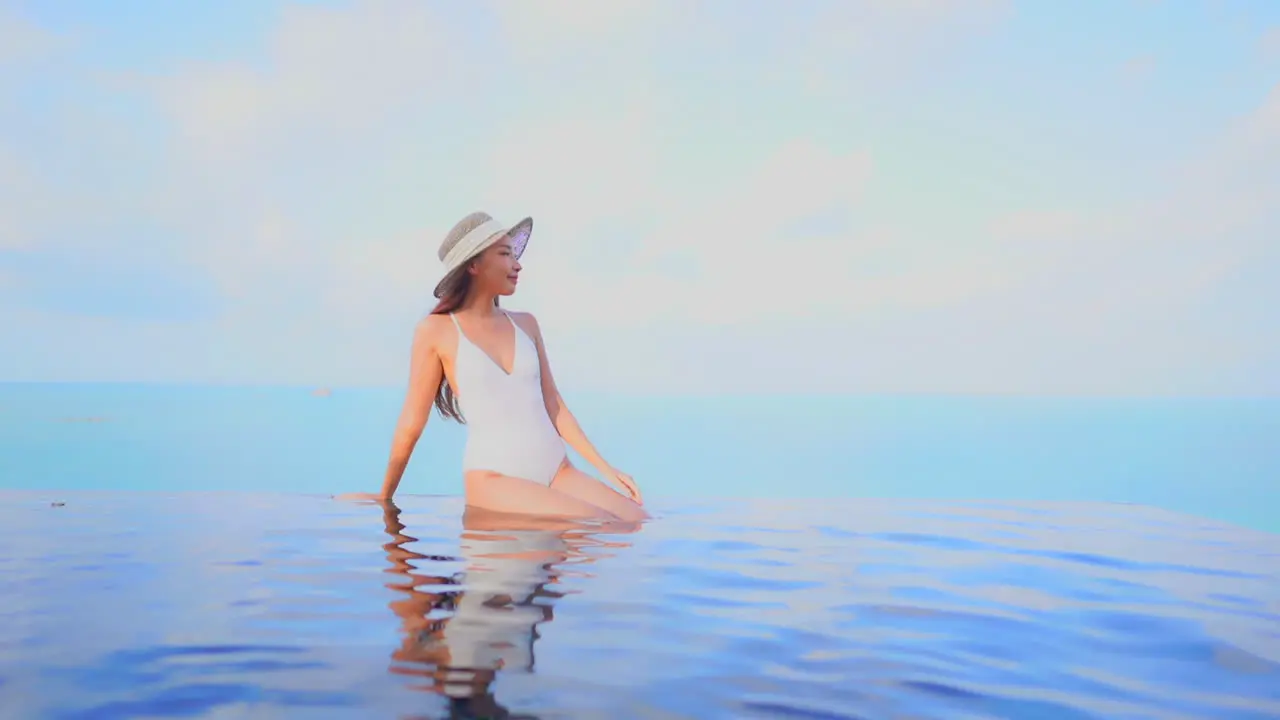 Stunning Asian model woman sitting at the edge of the infinity pool front view