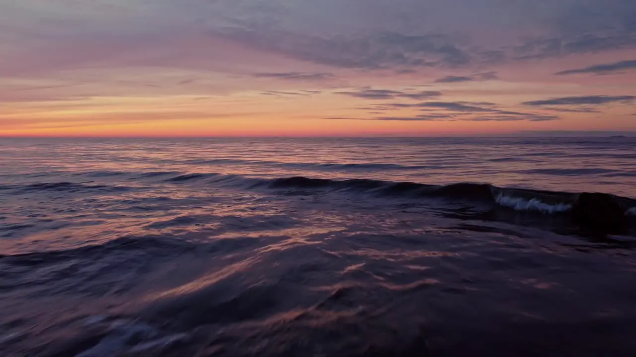 Low aerial drone flying above sea water waves at striking orange sunset sky