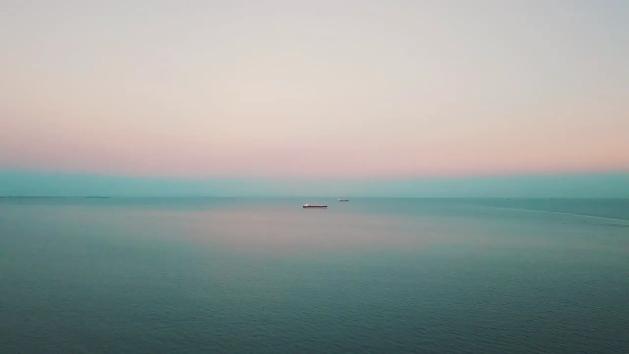 Drone flying above the sea with the cargo ship in the background at the sunset