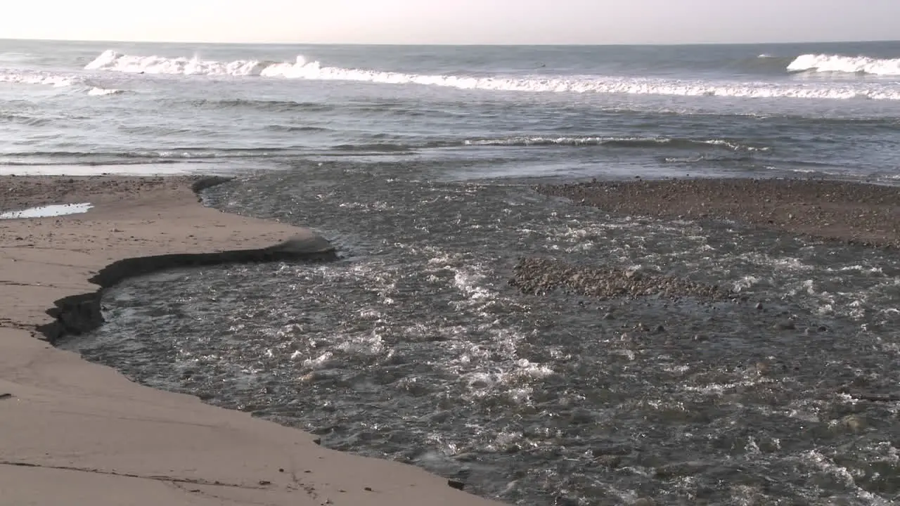 Surfer walking through water flowing out of the Ventura River estuary at Surfers Point in Ventura California