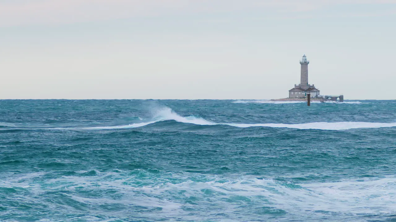 Waves creating crest on stormy weather with lighthouse Porer and cardinal mark