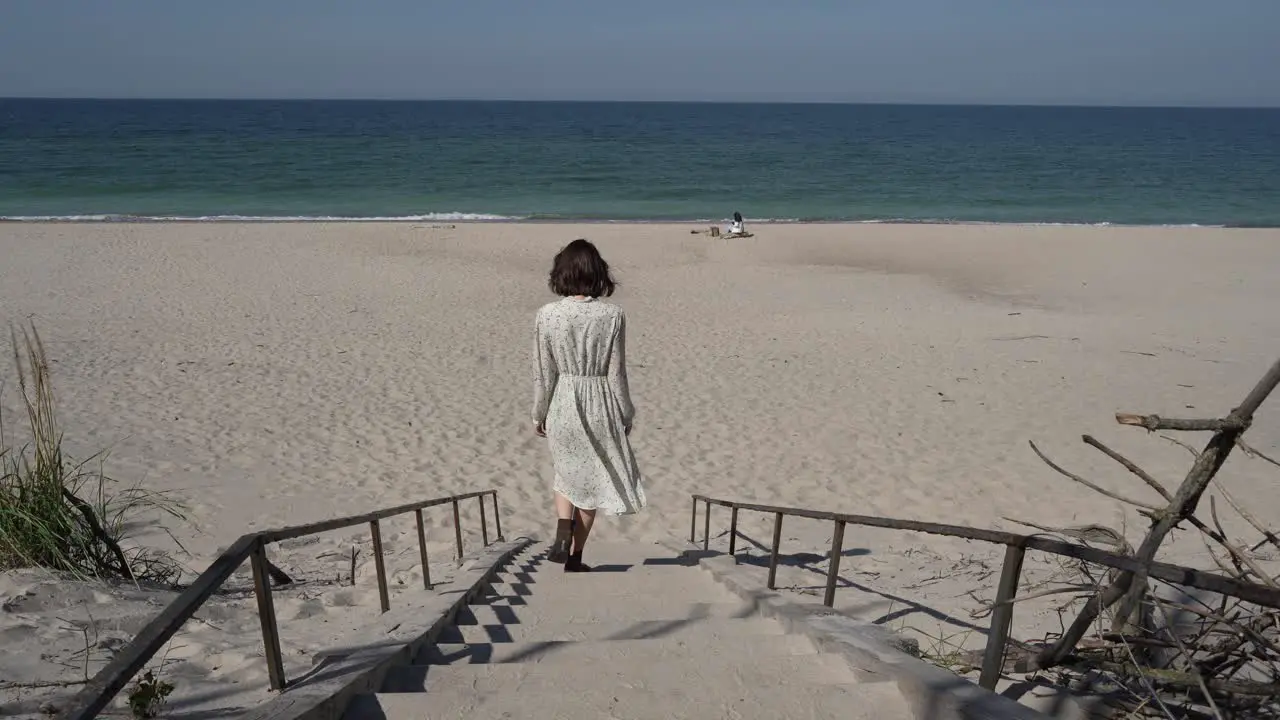 Girl with dark hair in white country dress goes down to the seaside by the wooden ladder