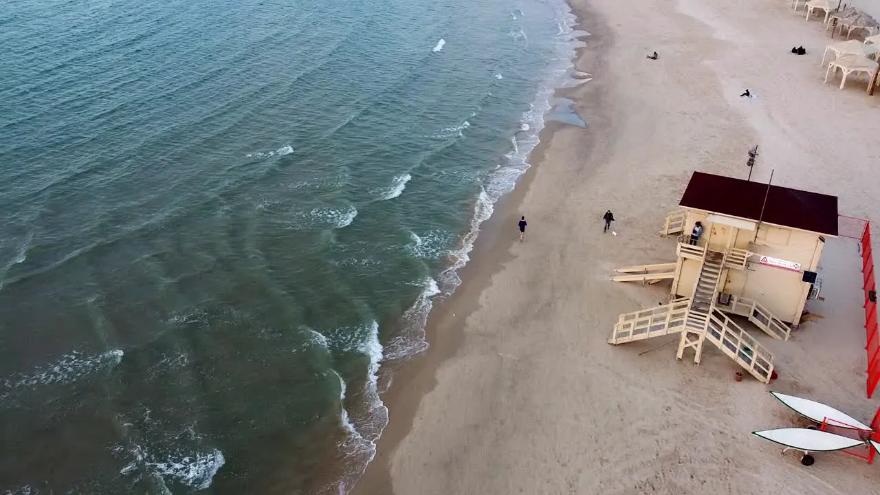 Aerial long shot follow man running at the beach lifeguard stand drone shot