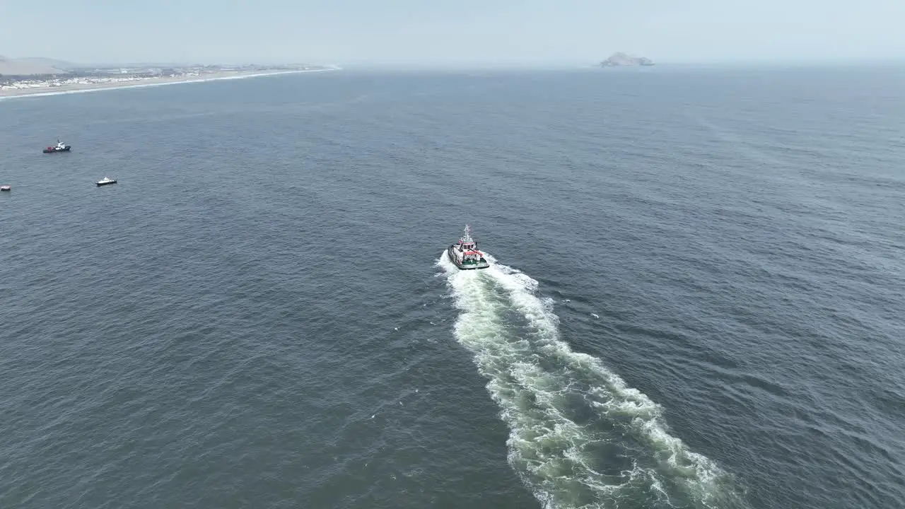 Aerial static shot with focus on a moving boat in the pacific ocean during calm waves in the sea with view of other boats and the beach of pucusuna beach in peru