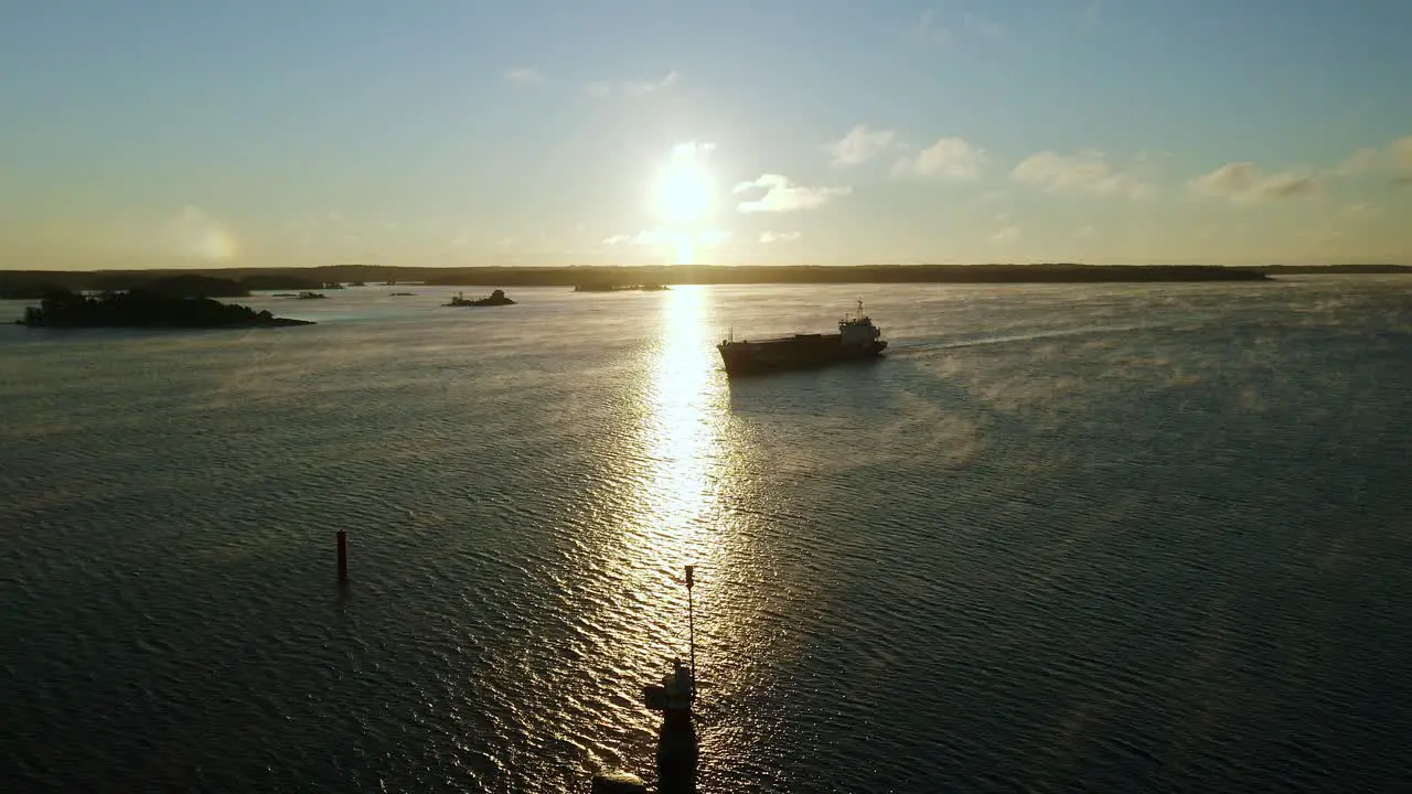 Aerial drone view of a general cargo vessel silhouette making way ahead during morning sunlight in finnish archipelago