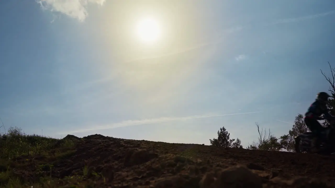 Low angle shot of cross motor bikes jumping over a hillock while driving along on a suuny day