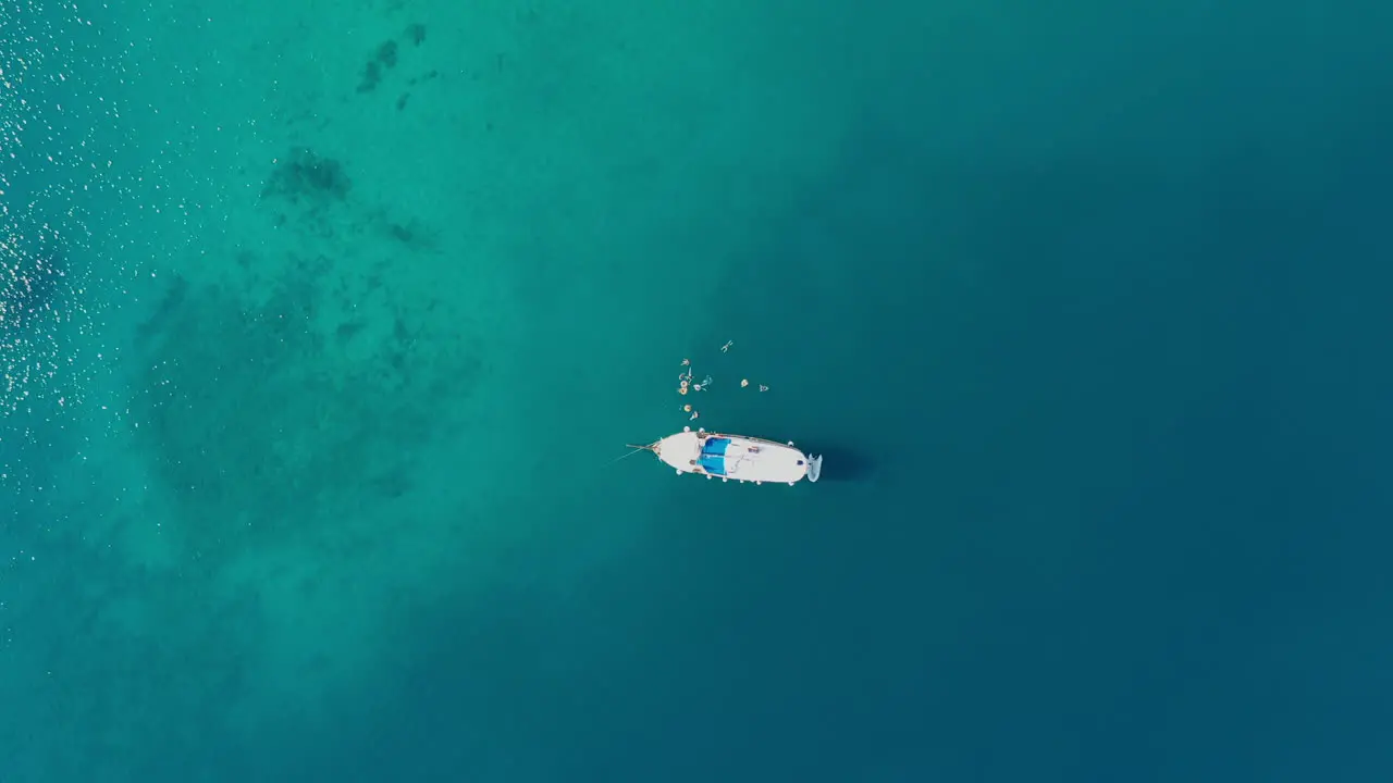 People swimming beside sailboat moored in tropical sea aerial top down view