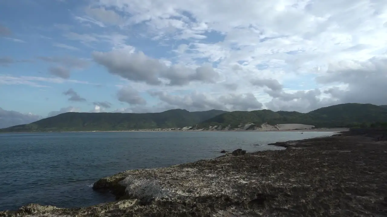 Rocky seashore with small mountains in the distance on slightly cloudy day