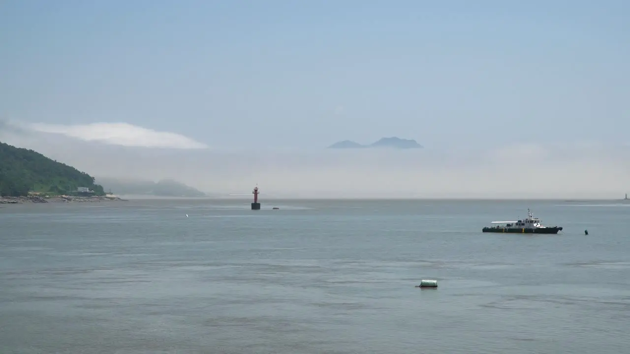 Fisherman's ship in the Yellow Sea and Red navigational buoy floating between islands a mountain covered in dense haze Ganghwado island South Korea static wide