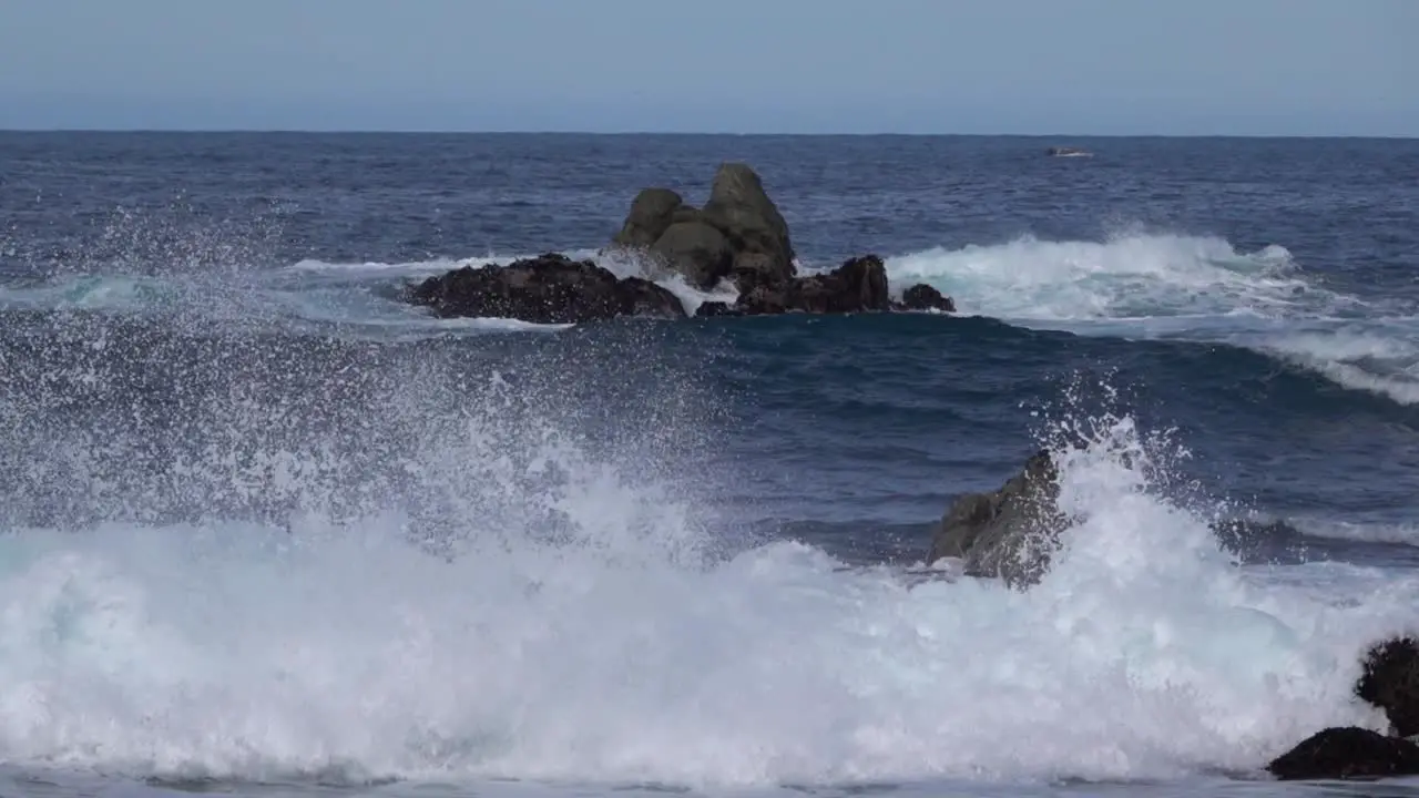 Incoming waves break violently on shore rocks splashing up sea foam