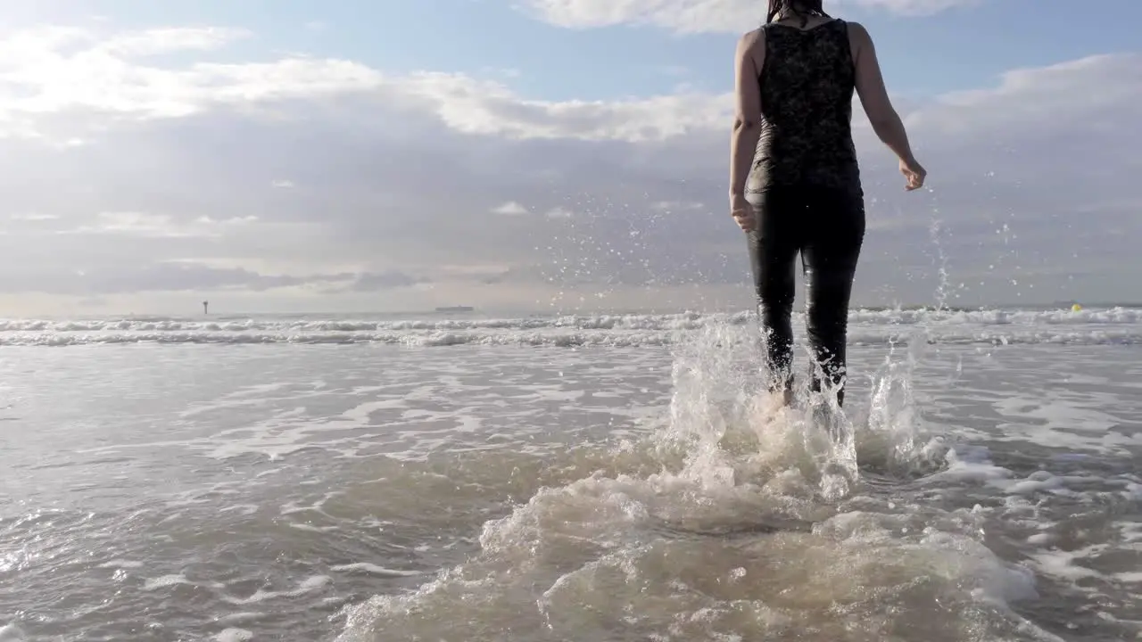 Tracking beach shot of a girl walking in the sea with feet splashing the gentle waves