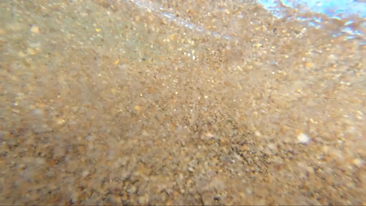 POV from within the surf being buffeted around within the waves surrounded by sand and bubbles and wave froth