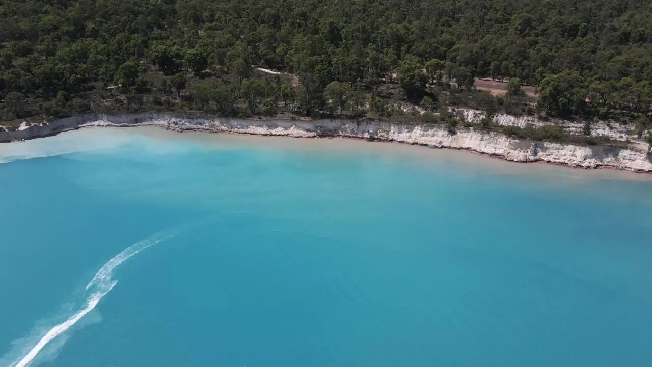 A dynamic aerial shot from a high altitude of the bay moving downward towards the seashore passing a fast jet ski leaving water trails behind