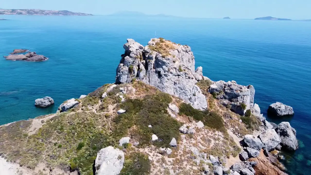 Cinematic aerial shot of a rock formation in a paradisiacal greek island with a small church on it