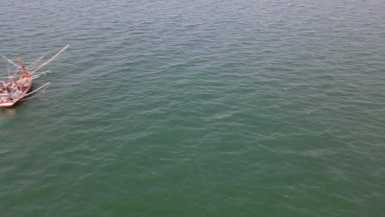 Aerial footage sliding to the left revealing a fishing boat in the middle of the ocean in Chonburi Thailand