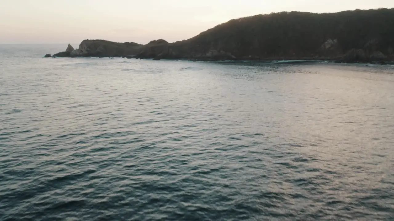 Drone tilt up shot of deep blue Pacific sea water leading upto the tip of land at sunset in Mazunte in Southern Mexico