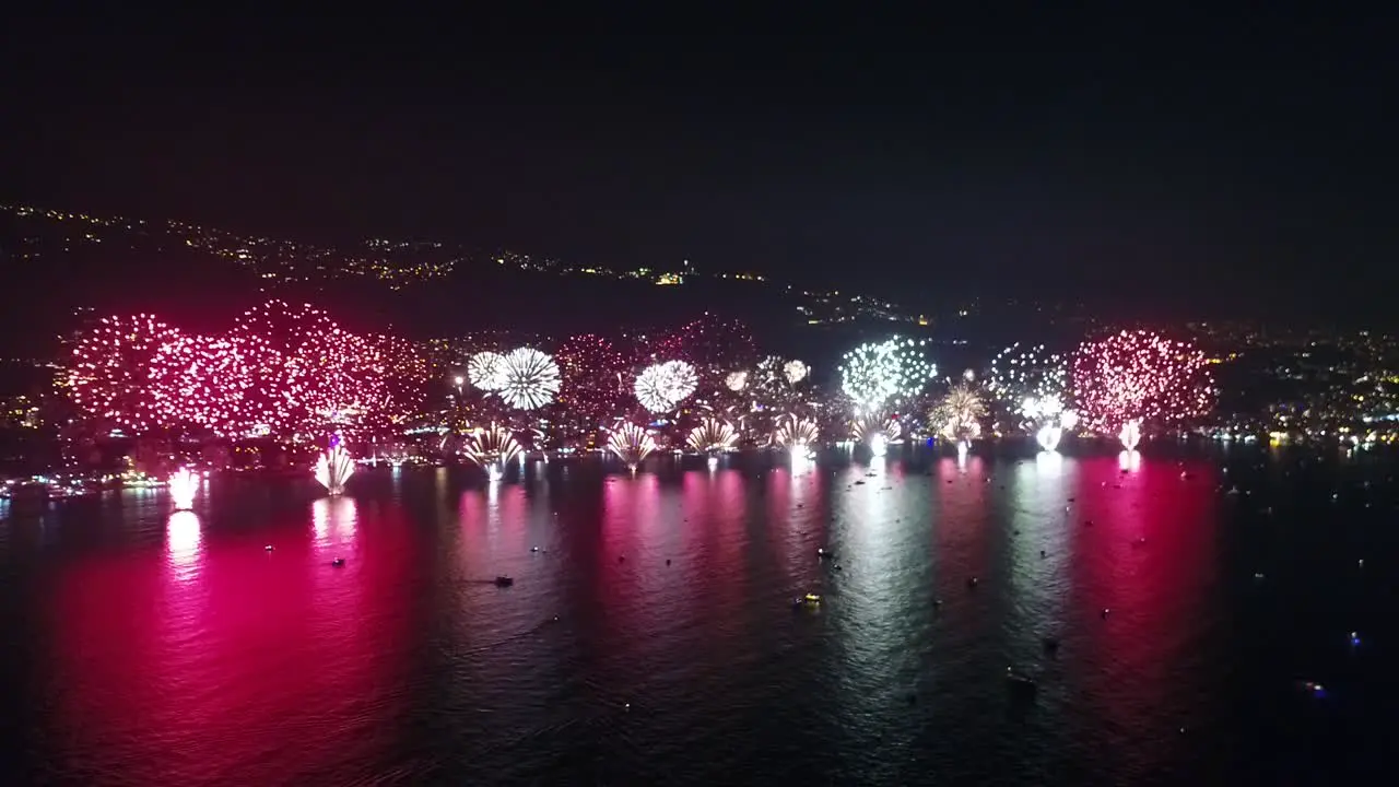 Fireworks lighting up city by the sea coast colorful light reflection on sea water new year celebration static aerial drone view night