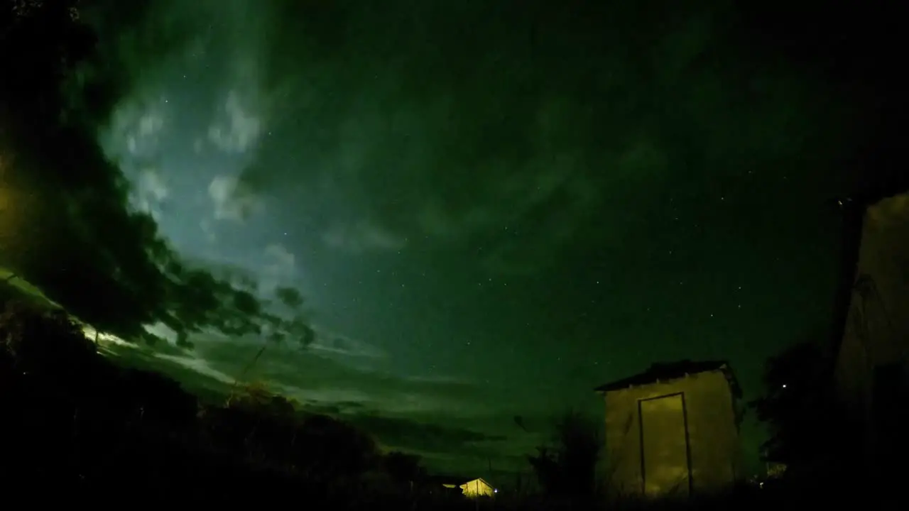 NIGHT LAPSE Stars and clouds view in a field with trees and little shack near by