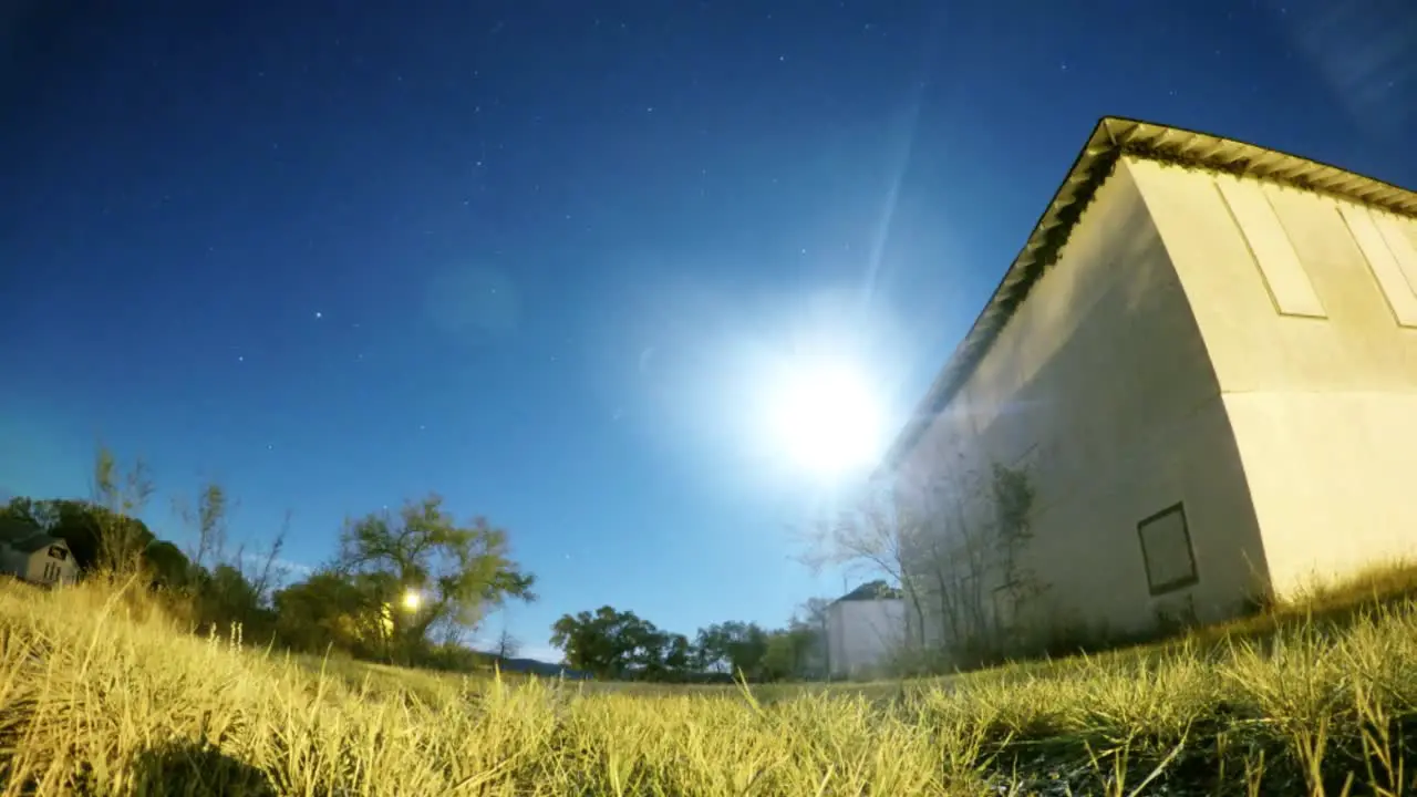 NIGHT LAPSE Blue sky with the moon and stars flying by a field with an old abandoned building