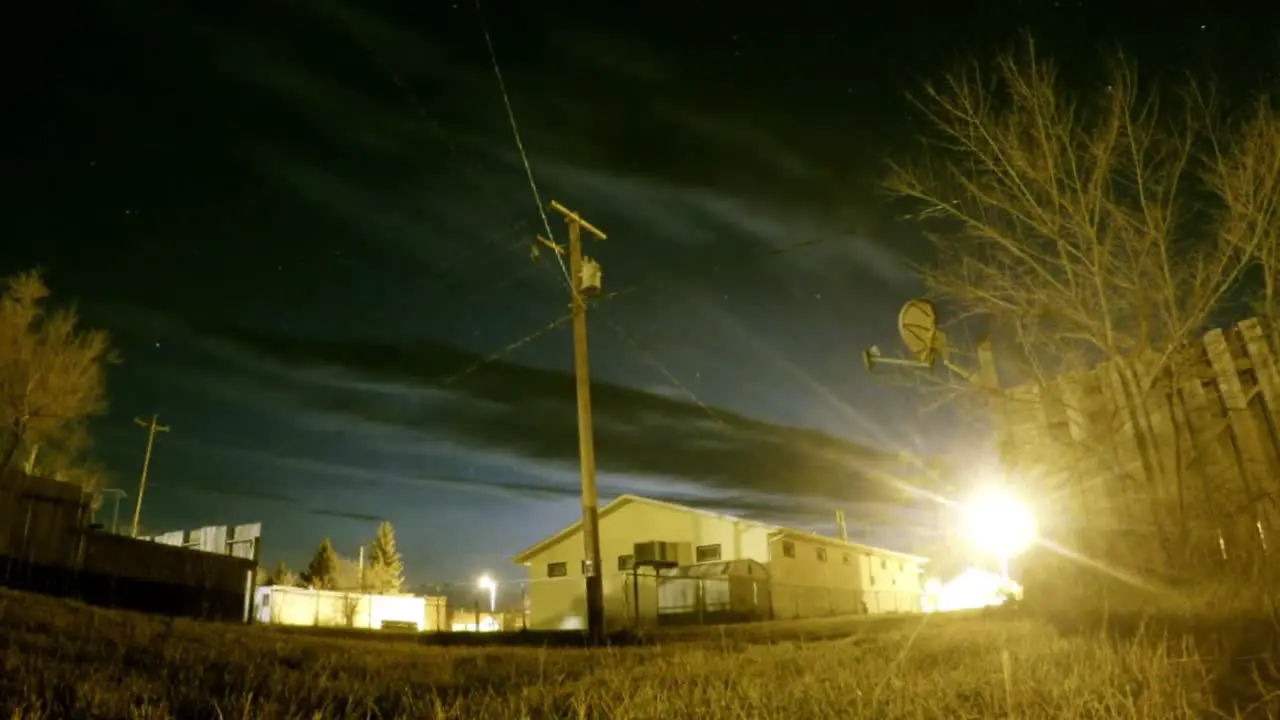 NIGHT NIGHT Clouds and stars in the night sky above a building with street lights and bushes around