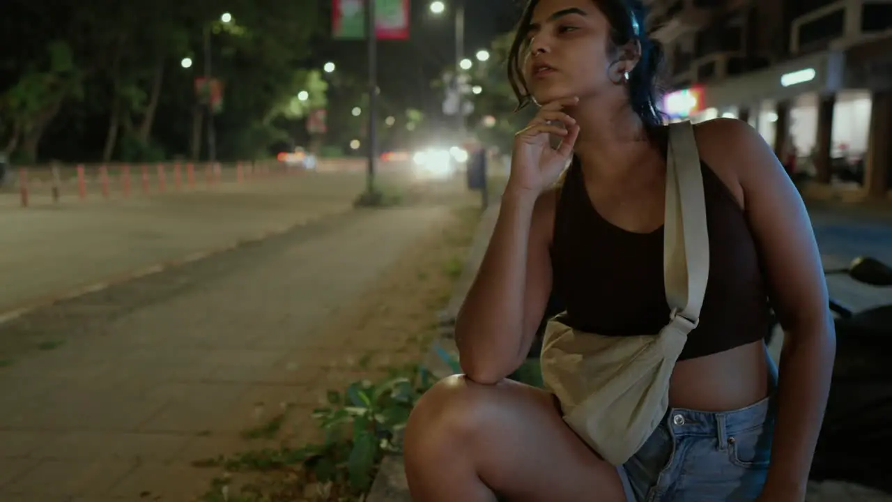 Fashionable Woman squatting on a sidewalk at night with city lights behind