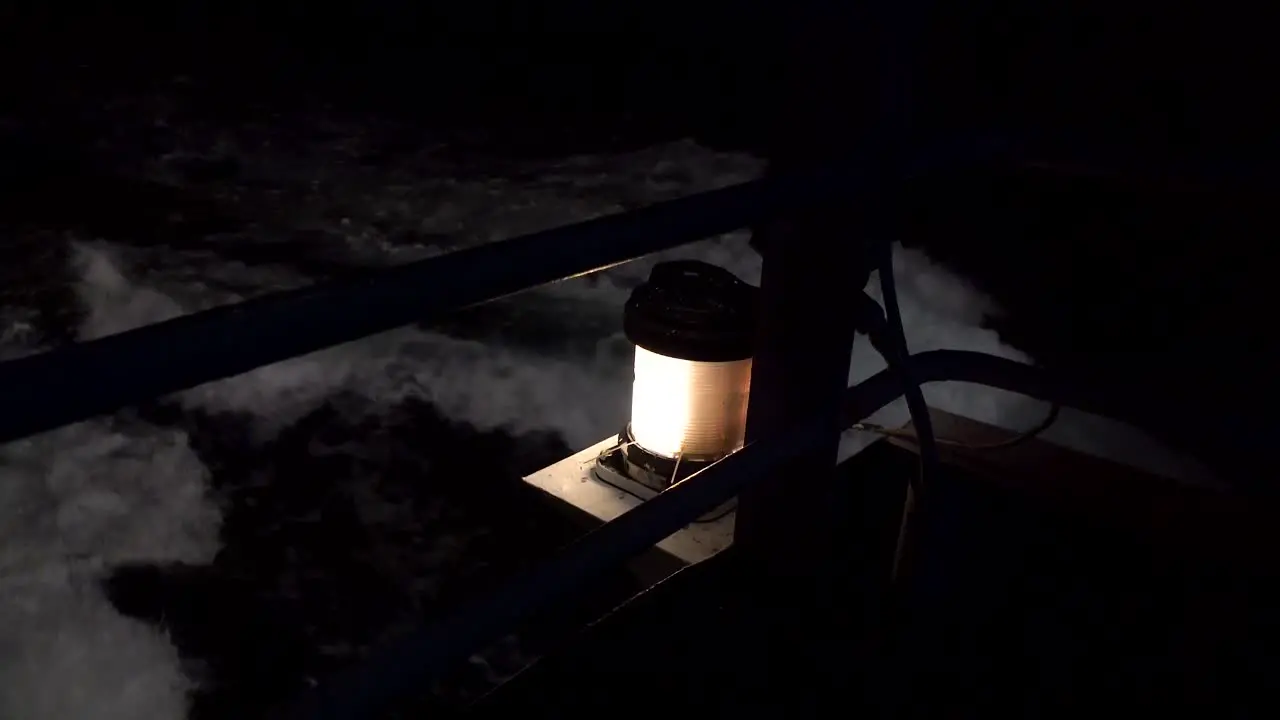 side view close up of yellow safety light shining in the dark night on ferry ship as rough black and white ocean waves pass by