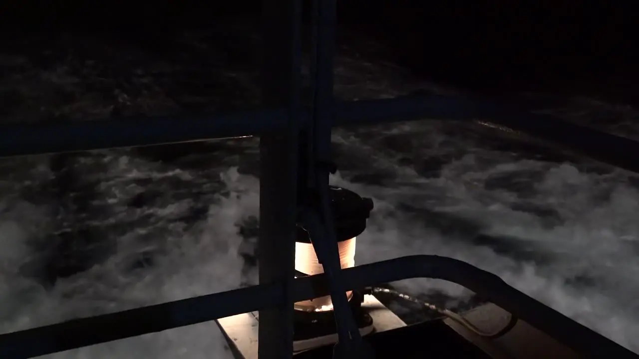 close up of yellow safety light on ferry ship as it sails through the dark night and white rough black and white ocean waves pass by