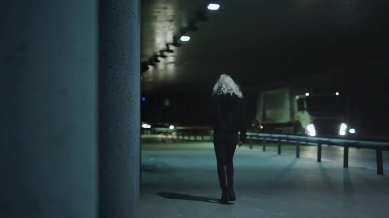 Woman walking away tunnel with driving cars at night city highway