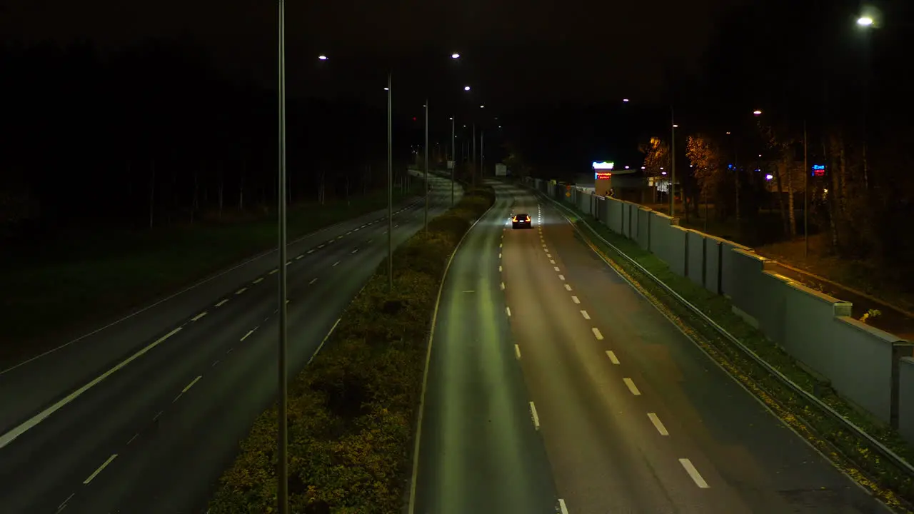 Black car driving alone on an empty highway at night