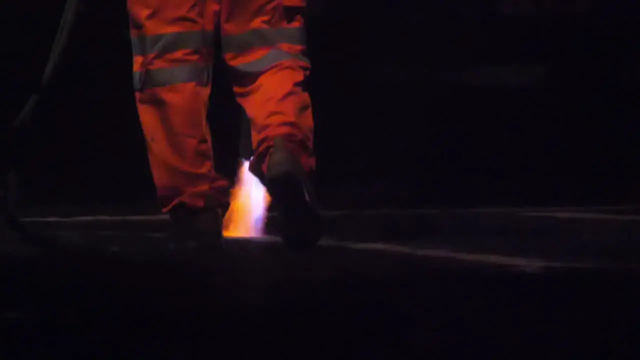 Slow motion view of a road worker using a Thermal lance to burn white lines from a main road before repainting at night