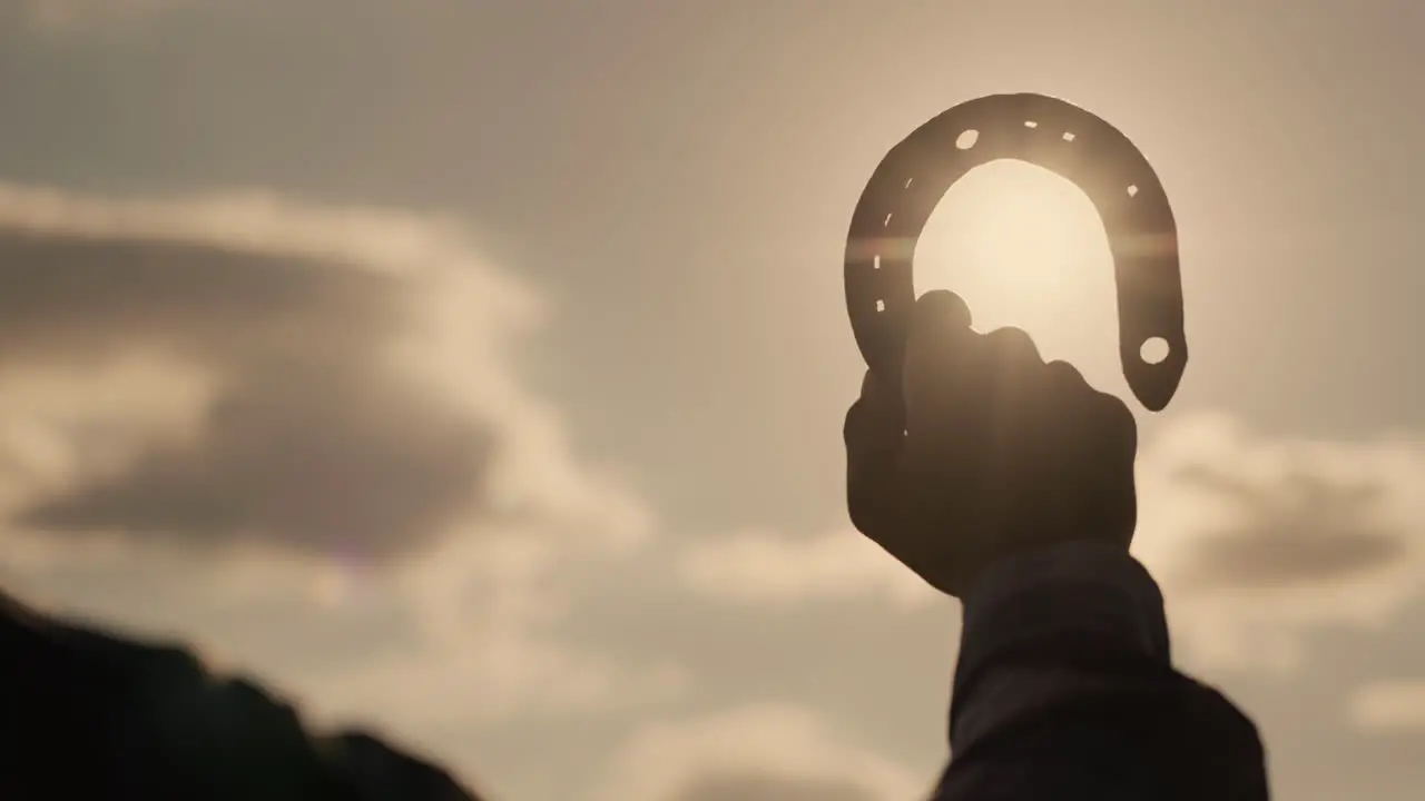 Hand of a man with a horseshoe against the sky and the sun