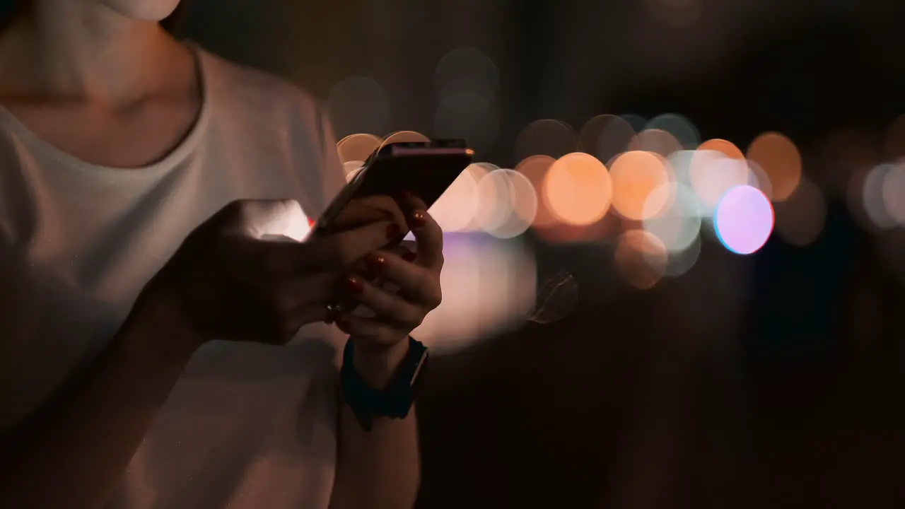 Close-up of a mobile phone in the hands of a girl presses her fingers on the screen in the night city on the background of a beautiful bokeh Young businessman girl