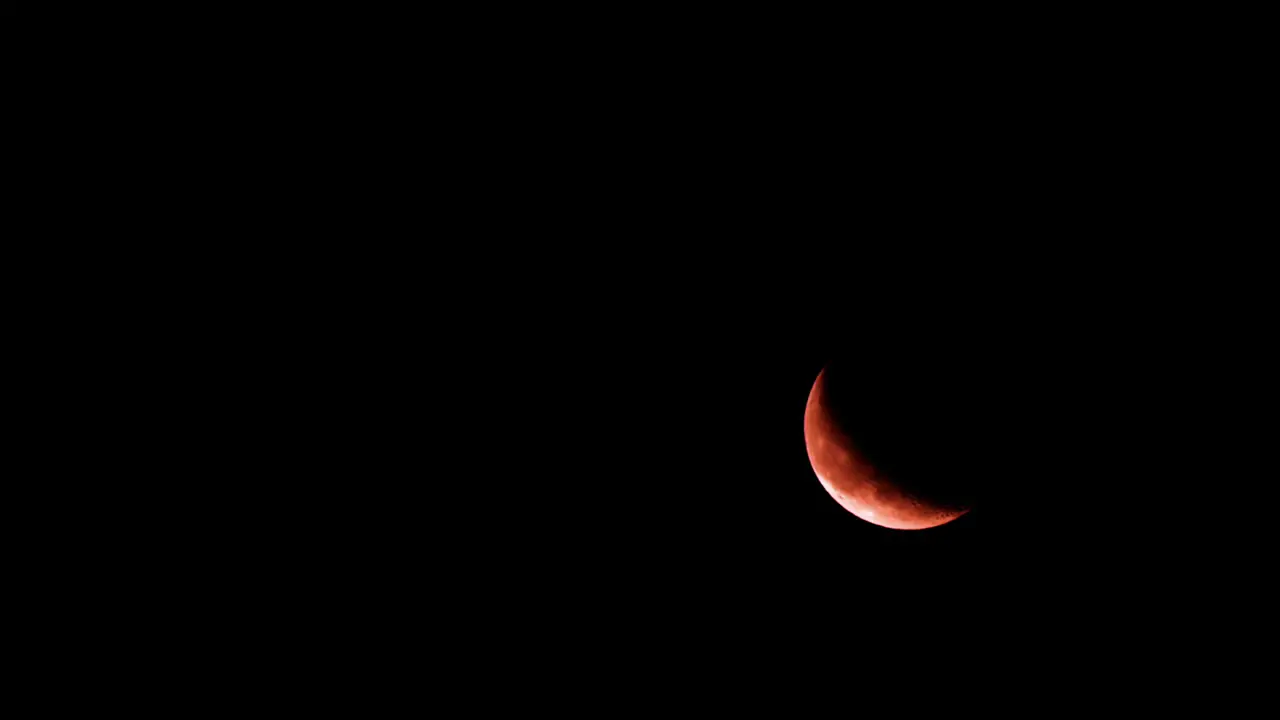 Bright crescent moon rises in lower right side of dark black night sky