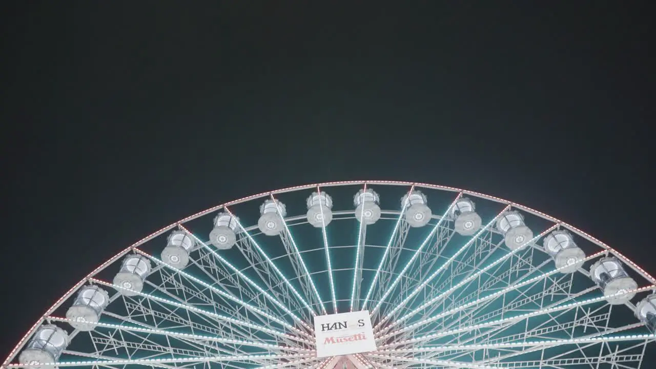 pan down over giant illuminated glowing ferris wheel at night time on Christmas market