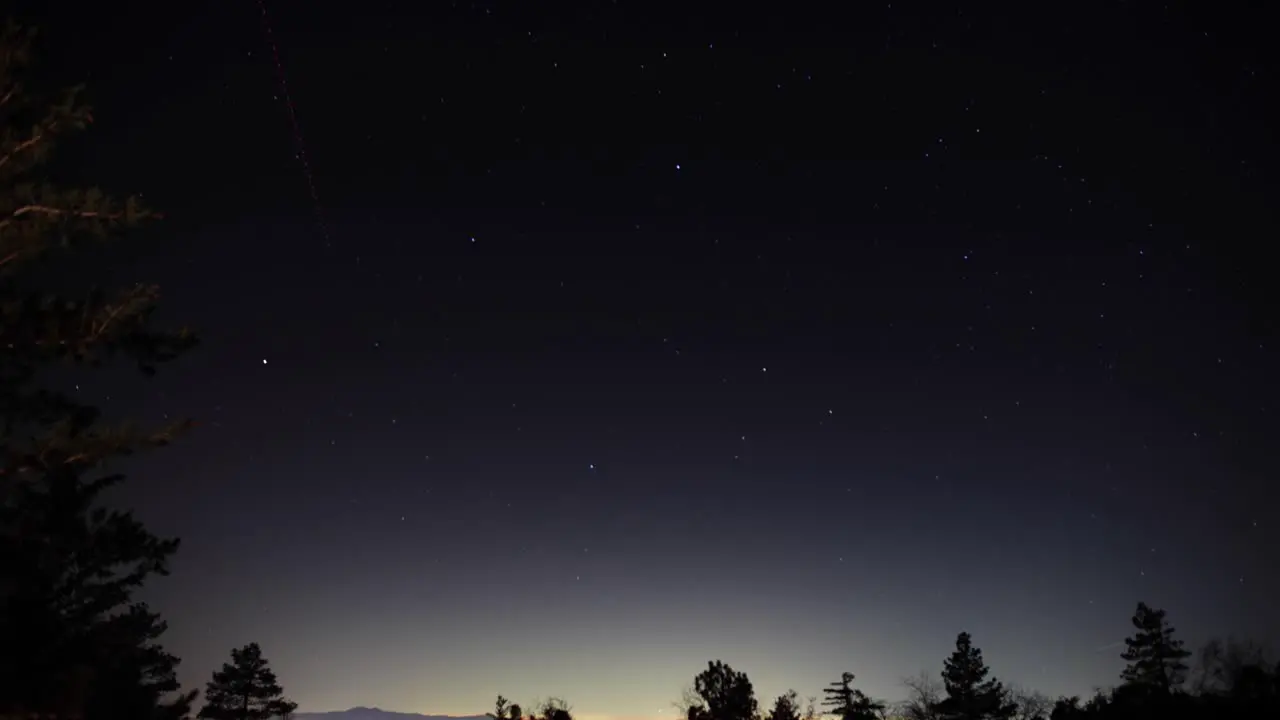 A stunning time-lapse of the stars moving over trees at night and shooting stars in the background