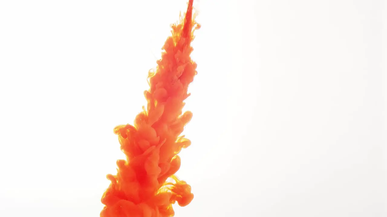 Against a plain white background a plume of orange colored liquid squirts down from above spreading out into a cloud over time