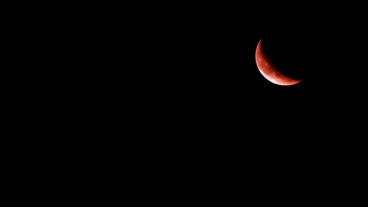 Glowing crescent moon rises in upper right of dark black night sky