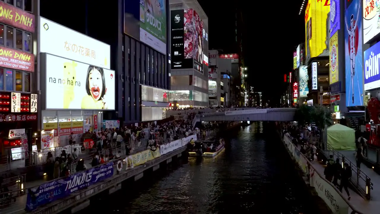 The Dotonbori bridge and canal at night time with people walking around the busy streets with billboards