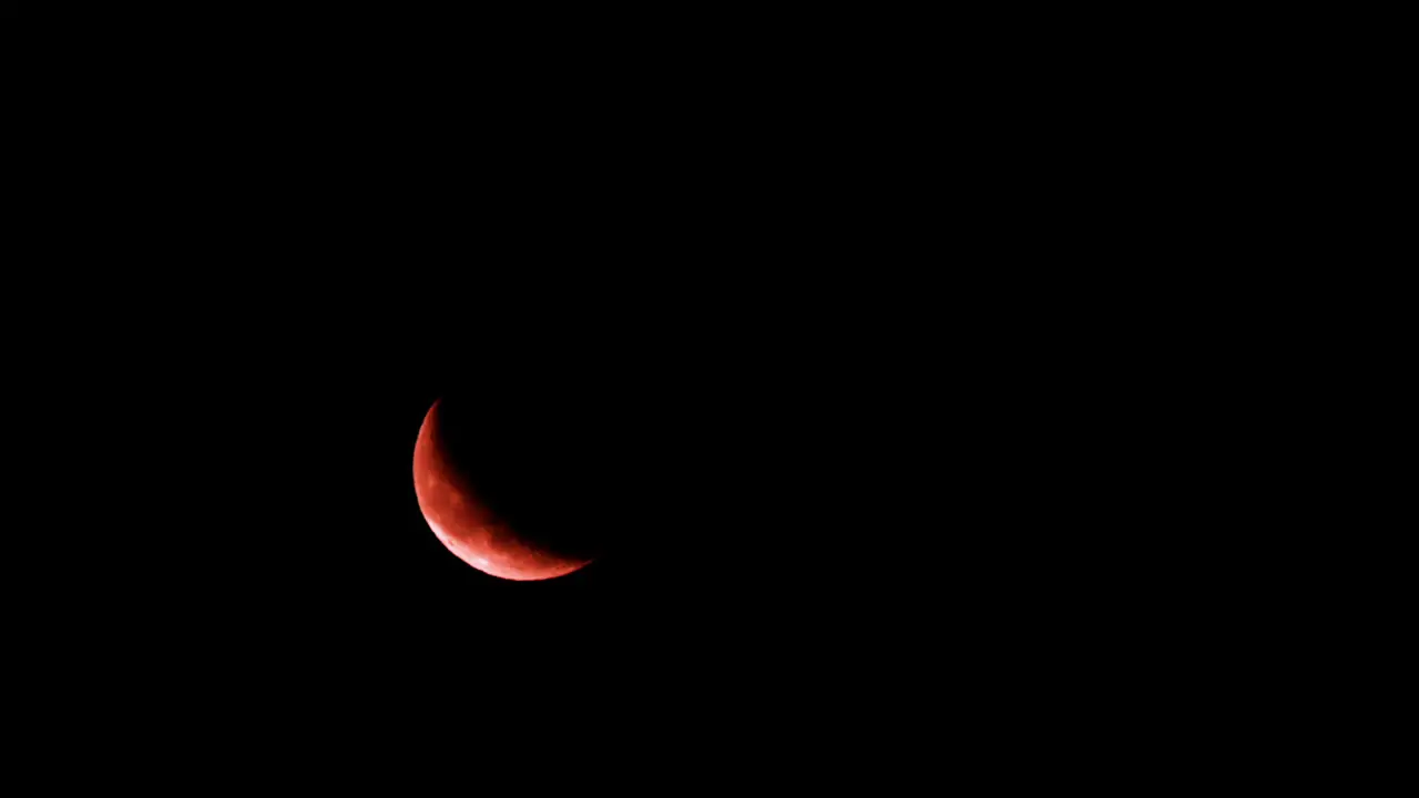 Orange crescent moon rises in lower left side of dark black night sky