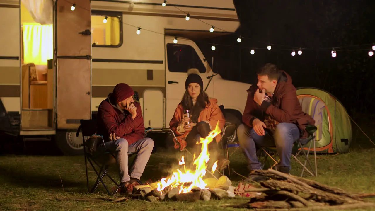 Group of friends gathered around camp fire in a cold night of autumn