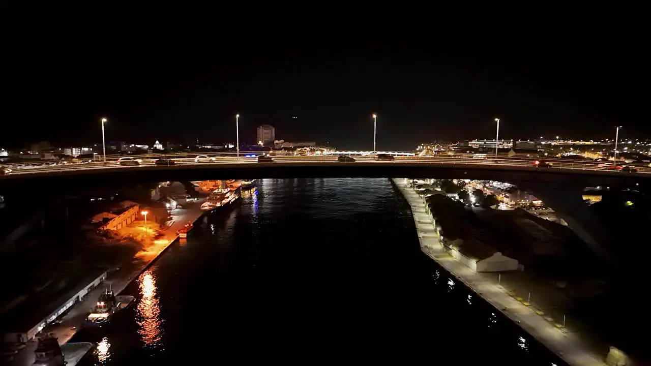 Cars rush over bridge at night as Willemstad comes into view at night aerial dolly