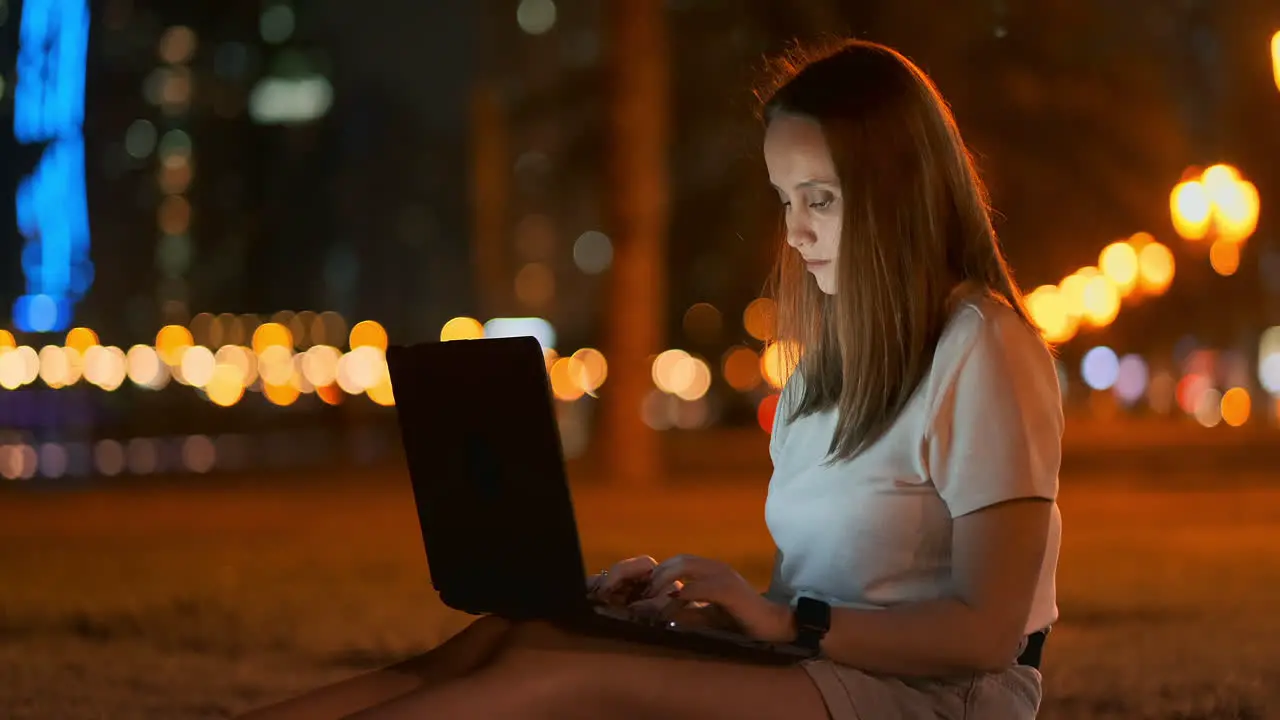 A young female student with a laptop at night in the city looking at the computer screen and typing with his hands on the keyboard Remote work on the Internet The student does the work Night life in the city