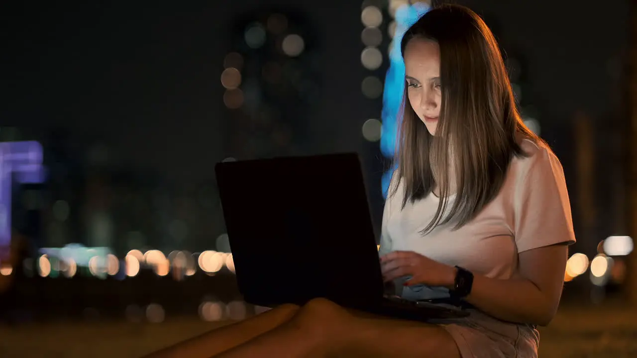 Young beautiful girl designer working remotely on a laptop on the street in the summer under palm trees at night in the city Park United Arab Emirates European woman at night in Dubai