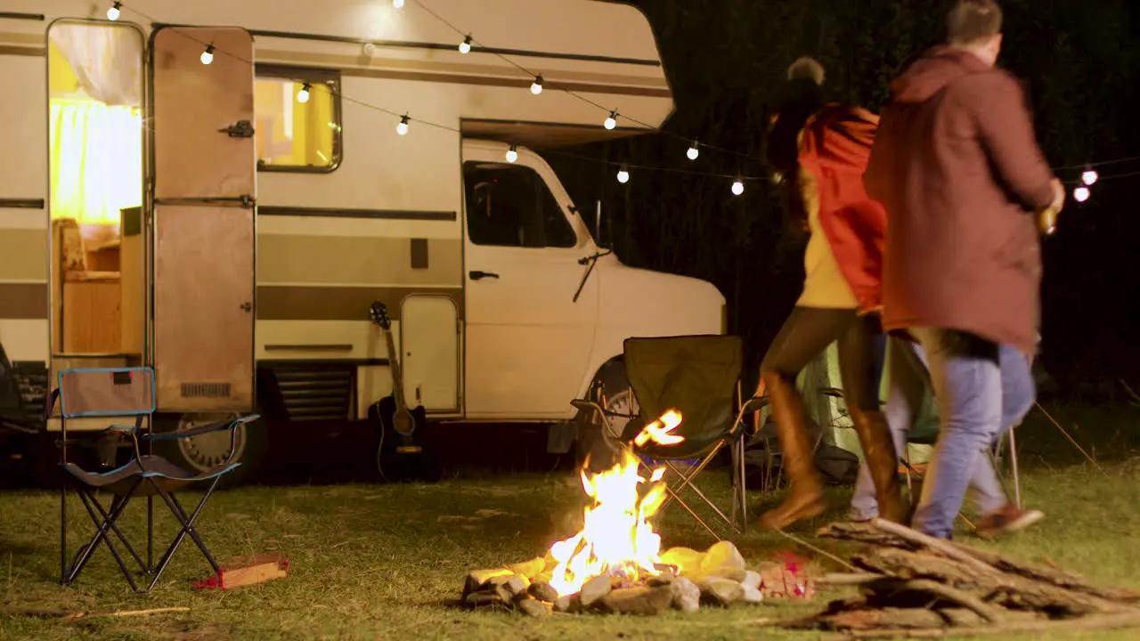 Group of close friends dancing around camp fire in a cold night of autumn