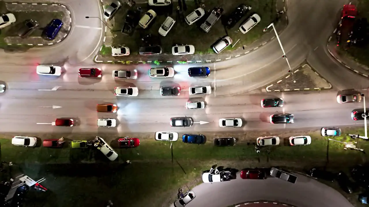 Cars lineup at traffic light crowded with vehicles parked on grass median aerial top down at night