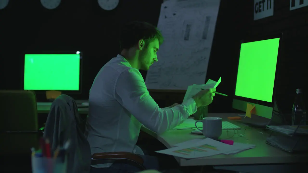 Young businessman working on computer with green monitor in night office