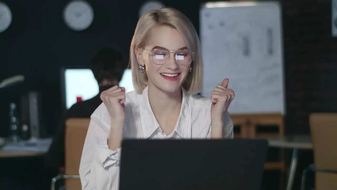 Satisfied business woman rejoicing good results front laptop in dark office